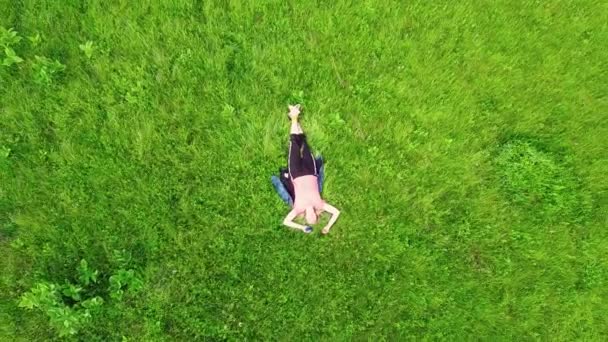 Point de vue aérien. Voler en orbite basse autour d'une fille allongée sur de l'herbe verte dans une merveilleuse clairière couverte d'herbe magique. Vêtements quotidiens et posture de méditation zen. Carpates, Ukraine — Video