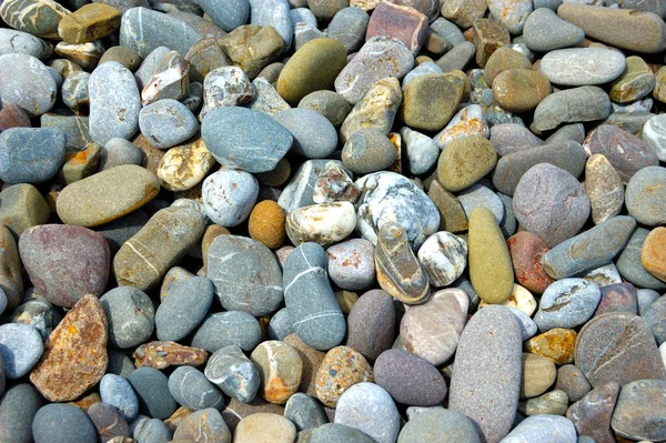 Playa de guijarros de mar con piedras multicolores, olas transparentes con espuma, en un cálido día de verano — Foto de Stock