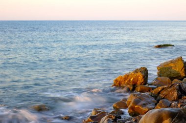 Karadeniz 'de gün batımı. Güzel bulutlar, mavi gökyüzü, ufukta güneş. Ön planda güzel taşlar
