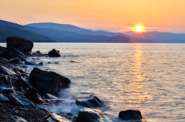 Karadeniz 'de gün batımı. Güzel bulutlar, mavi gökyüzü, ufukta güneş. Ön planda güzel taşlar