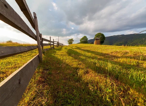 Petite vieille clôture en bois située sur une colline verte. Sur fond montagnes et ciel bleu clair sans nuages — Photo
