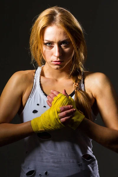 Muscular young athletic sportswoman in sportswear with bands or gloves in the gym on a dark background. Sports martial arts. Copy space for ads for fitness nutrition, sports equipment or exercise. — Stock Photo, Image
