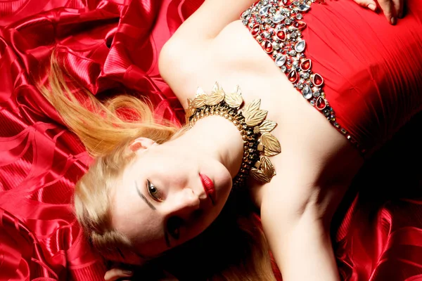 Elinde buketi olan, taç takmış güzel bir sarışın. Parkta yeşil, büyük ve gür kırmızı bir elbise giymiş.