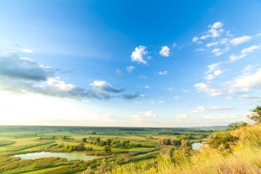 Nehiri olan güzel bir vadi, büyük bulutları ve parlak güneşi olan mavi bir gökyüzü. Hava 4K UHD
