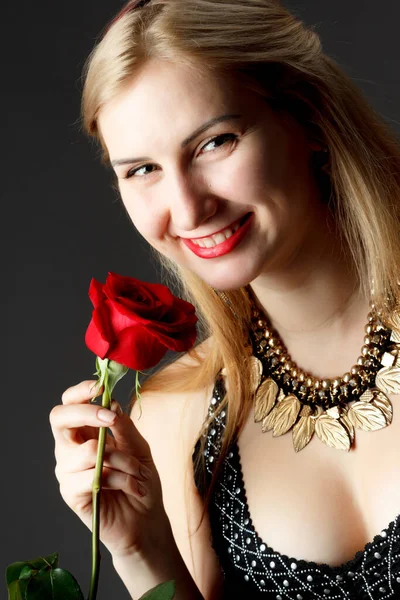 Vackra glad tjej innehar röd ros nära ansiktet och ser på kameran. — Stockfoto