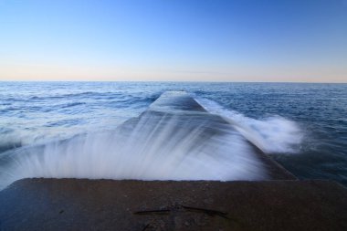 Devasa bir dalgakıran denizin derinliklerine çarpıyor ve deniz kıyılarını denizin elementlerinden koruyor. Denizde harika bir gün batımı. Kırım 'ın saf ve harika doğası. Ukrayna.
