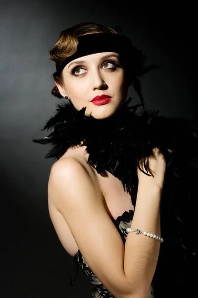 Portrait of a glamorous dark haired model with perfect makeup wearing a luxurious necklace, black bodysuit and long top, holding her hands behind her head and looking straight ahead. Stock Photo