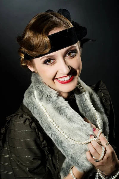 Mükemmel makyajlı, şaşaalı koyu renk saçlı bir mankenin portresi. Şık bir kolye, siyah bir kıyafet ve uzun bir bluz giyiyor. Ellerini başının arkasında tutuyor ve ileriye bakıyor..