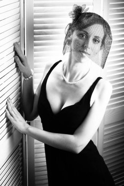 Siyah elbisesi ve yüksek topuklu ayakkabıları olan, uzun saçlı, esmer, güzel bir kadın beyaz arka planda yürüyor. Güzellik, cinsellik, şık kıyafetler. Tam boyut, boşluğu kopyala