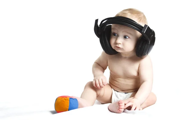 Beau bébé mignon sourit et écoute de la musique dans des écouteurs noirs sur un fond blanc. Éducation des enfants. Photos De Stock Libres De Droits