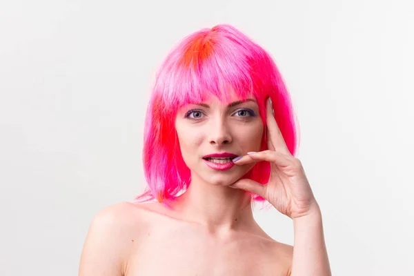 Imagen de la hermosa mujer excitada en la peluca riendo mientras posando con dulces aislados sobre fondo rosa — Foto de Stock