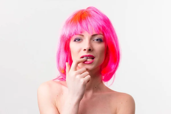 Imagen de la hermosa mujer excitada en la peluca riendo mientras posando con dulces aislados sobre fondo rosa —  Fotos de Stock
