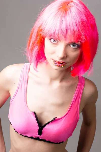 Изображение возбужденной красивой женщины в парике смеясь во время позирования с конфеты изолированы на розовом фоне — стоковое фото