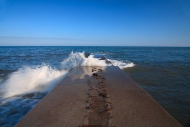 Devasa bir dalgakıran denizin derinliklerine çarpıyor ve deniz kıyılarını denizin elementlerinden koruyor. Denizde harika bir gün batımı. Kırım 'ın saf ve harika doğası. Ukrayna.