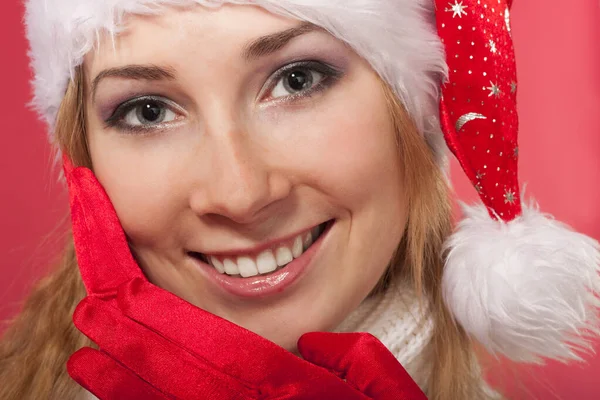 Beautiful young woman in santa claus hat and mittens smiling. Christmas tale. Red background. Postcard. Space for text. — Stock Photo, Image