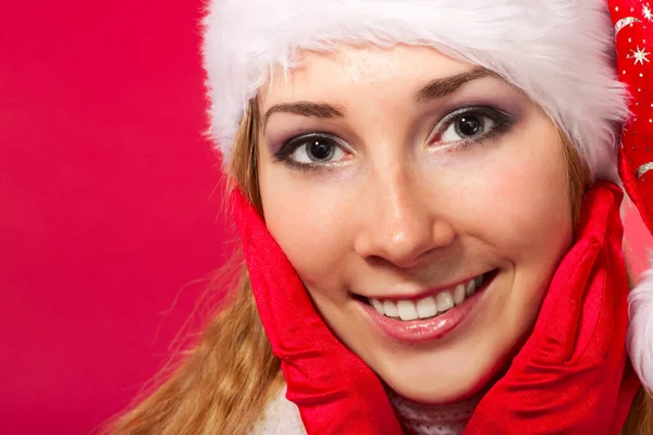Beautiful young woman in santa claus hat and mittens smiling. Christmas tale. Red background. Postcard. Space for text. — Stock Photo, Image