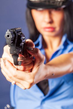 Stüdyoda silahlı üniformalı bir kız poz veriyor. Vurgu, ön planda yer alan silahta..