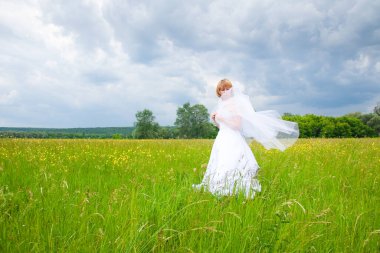 Düğün günü, güzellik, doğa konsepti. Tarlanın ortasında beyaz gelinlik giyen harika bir kadın var. Kendi etrafında dönüyor ve pullar güneşin ışığında parlıyor.