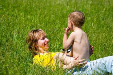 Genç anne ve bir yaşındaki kızı parkta çimlerin üzerinde dinleniyorlar. Aile birlikte eğleniyor.. 