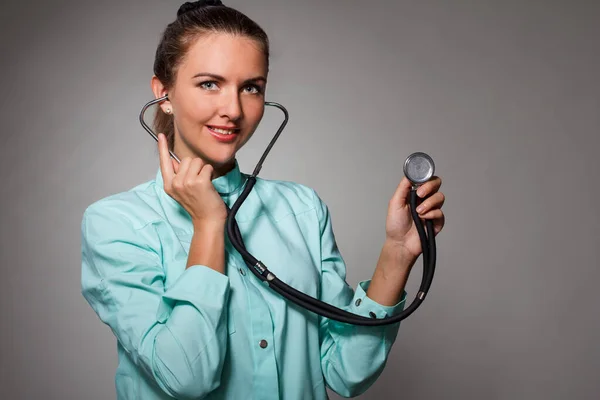 Smärta i bröstet. Fokuserad säker kvinnlig läkare som använder stetoskop samtidigt diagnostisera hälsa och poserar på den isolerade bakgrunden — Stockfoto