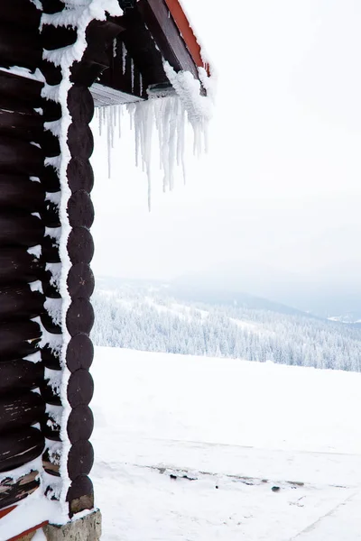 A casa de logs com o gelo sobre o telhado e pendurado para baixo icicles. — Fotografia de Stock