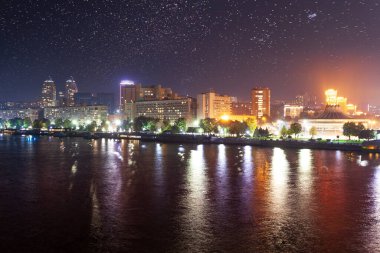 Modern yüksek binalar, gökdelenler ve şehir ışıklarıyla soyut şehir manzarası karanlık bir gecede sakin nehir veya gölün ayna su yüzeyine yansıyor. İnsansız..