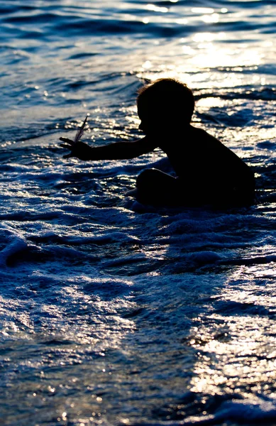 Silhouette of a child walking into the blue glittering sea in moonlight - Stok İmaj