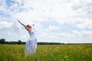 Düğün günü, güzellik, doğa konsepti. Tarlanın ortasında beyaz gelinlik giyen harika bir kadın var. Kendi etrafında dönüyor ve pullar güneşin ışığında parlıyor.