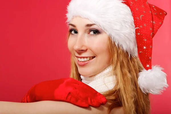 Piękna młoda kobieta w kapeluszu Świętego Mikołaja i rękawicach uśmiechnięta. Świąteczna historia. Czerwone tło. Pocztówka. Miejsce na tekst. — Zdjęcie stockowe
