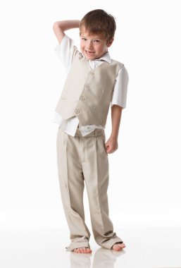 A handsome little boy dressed as a schoolboy - in a white shirt and gray trousers, stands against a white wall and poses, jumps like a model. isolated on white background.