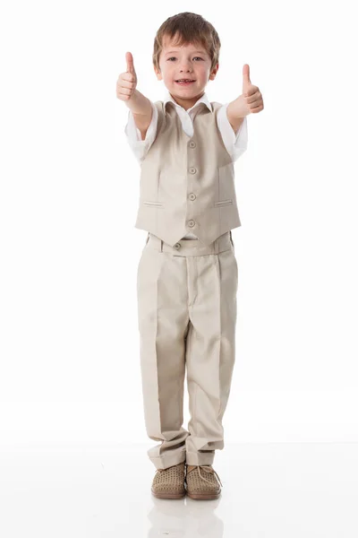 Um garotinho bonito vestido de estudante - com uma camisa branca e calças cinzas, encosta-se a uma parede branca e posa, pula como um modelo. isolado em fundo branco. — Fotografia de Stock