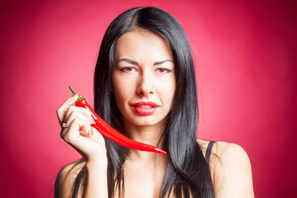 Bella donna in lingerie di pizzo nero in posa in studio con sfondo rosso. Sta giocando con il peperoncino.. — Foto Stock