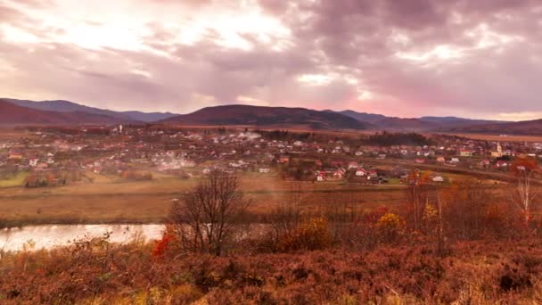 Veduta aerea di case di paese in una valle di montagna contro un cielo blu con nuvole occasionali. Villaggio di montagna incastonato tra alte colline ricoperte di boschi verdi. — Video Stock