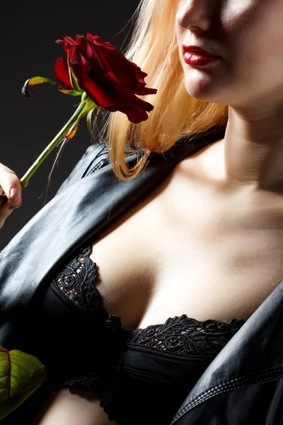 Retrato de modelo de mujer joven en vestido rojo sosteniendo flor de rosa roja en la mano sobre fondo oscuro en el estudio de fotografía. Concepto de belleza y moda — Foto de Stock