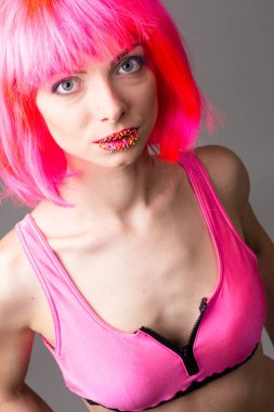 Pembe arka planda izole edilmiş şekerlerle poz veren peruklu güzel bir kadının görüntüsü