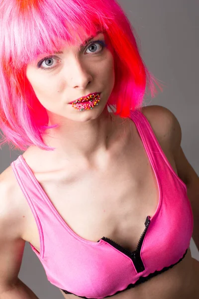 Pembe arka planda izole edilmiş şekerlerle poz veren peruklu güzel bir kadının görüntüsü