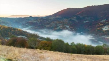Sonbahar dağlarında güneşin doğuşunda destansı bir uçuş. Sarı ve kırmızı sonbahar ağaçları, arka planda sabah sisi. Sonbahar doğa ormanı geçmişi