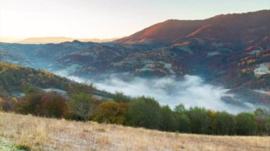 Sonbahar dağlarında güneşin doğuşunda destansı bir uçuş. Sarı ve kırmızı sonbahar ağaçları, arka planda sabah sisi. Sonbahar doğa ormanı geçmişi