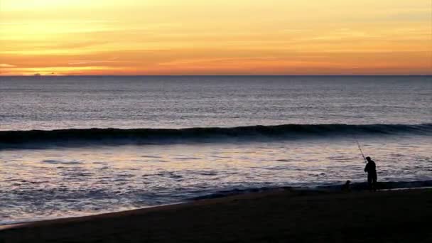 Silhouet van de mens vissen at dusk in vale do lobo beroemde strand, algarve, portugal. — Stockvideo