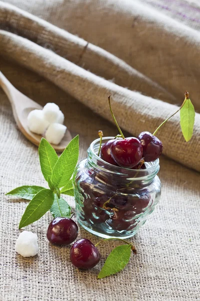 Cerezas rojas en frasco de vidrio sobre tela de saco — Foto de Stock