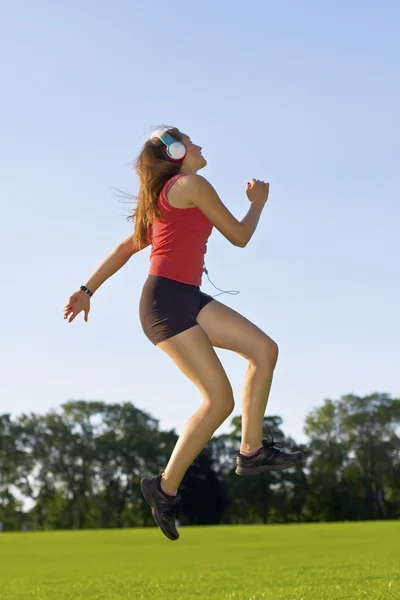 Fille heureuse écouter de la musique sauter dans le parc, profiter de la musique — Photo