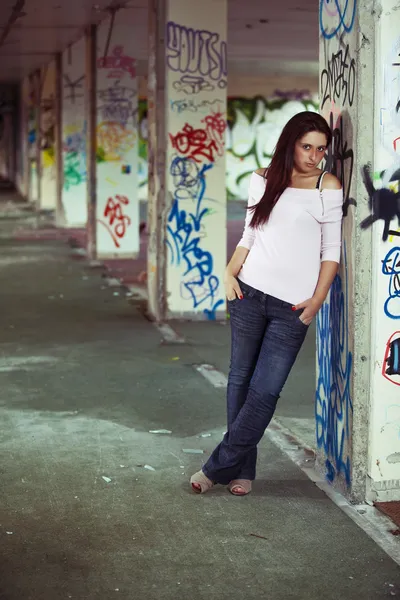Jonge mooie meisje poseren in verlaten graffiti geschilderd gebouw — Stockfoto