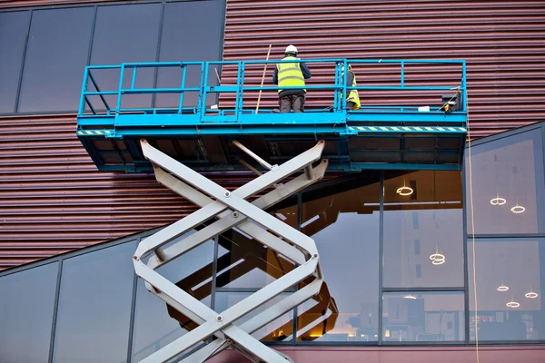 Constructor en una plataforma de elevación de tijera en un sitio de construcción —  Fotos de Stock