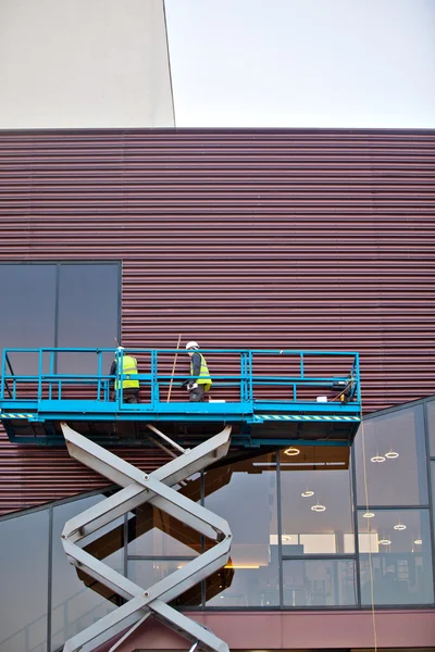 Constructor en una plataforma de elevación de tijera en un sitio de construcción — Foto de Stock