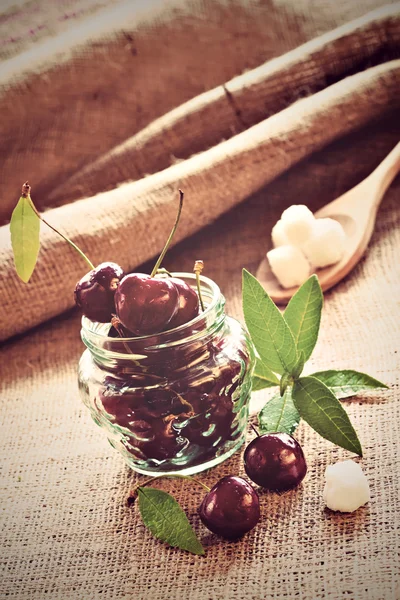 Cerezas rojas en frasco de vidrio sobre tela de saco — Foto de Stock