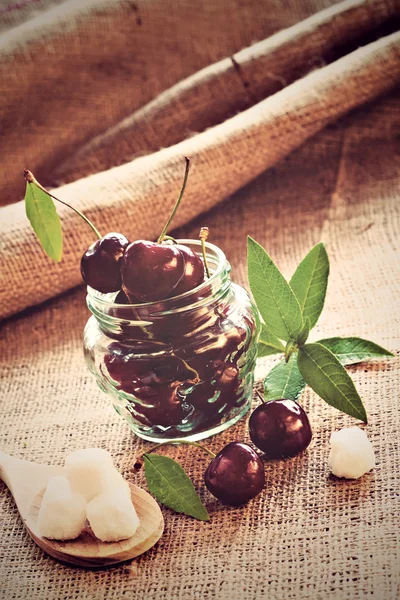 Red cherries in glass jar on sackcloth — Stock Photo, Image