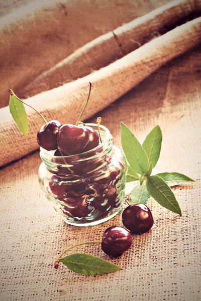 Red cherries in glass jar on sackcloth — Stock Photo, Image