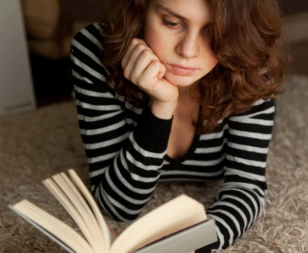 Mujer joven leyendo un libro acostado en la alfombra, en un enfoque suave —  Fotos de Stock
