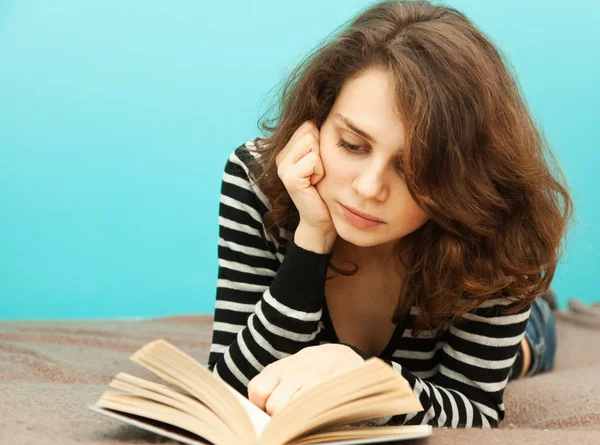 Jovem mulher lendo um livro deitado, em foco suave — Fotografia de Stock