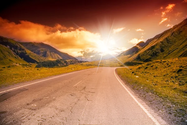 Vägen i berg landskap med ljusa solnedgång himlen — Stockfoto